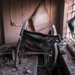 Tra i resti del centro, il primo piano di una sedia a rotelle danneggiata Tra i resti del centro, il primo piano di una sedia a rotelle danneggiata