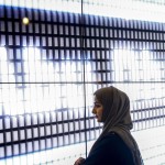 Una donna davanti al display con su scritto Abu Dhabi, capitale degli Emirati Arabi Uniti