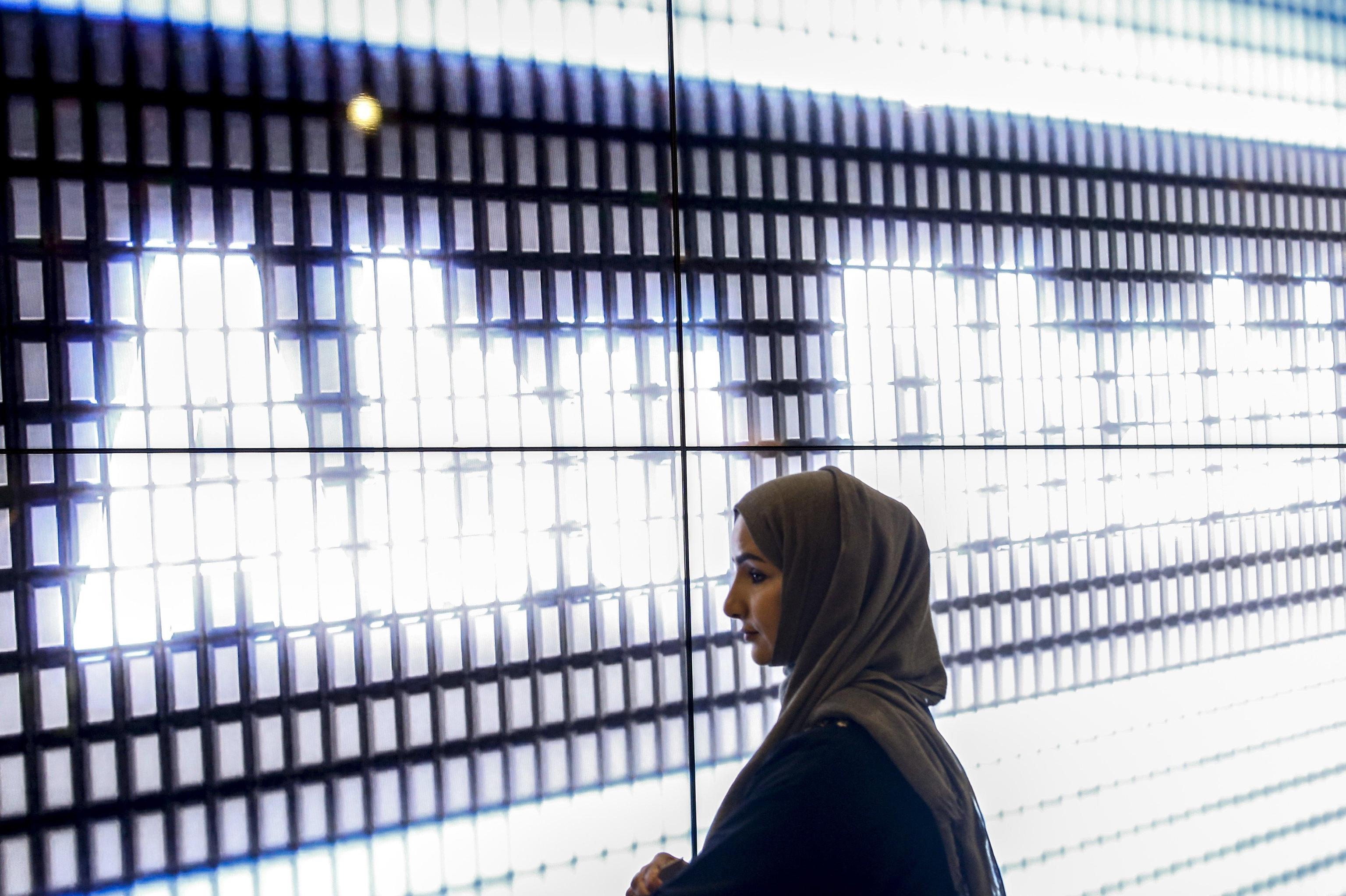 Una donna davanti al display con su scritto Abu Dhabi, capitale degli Emirati Arabi Uniti