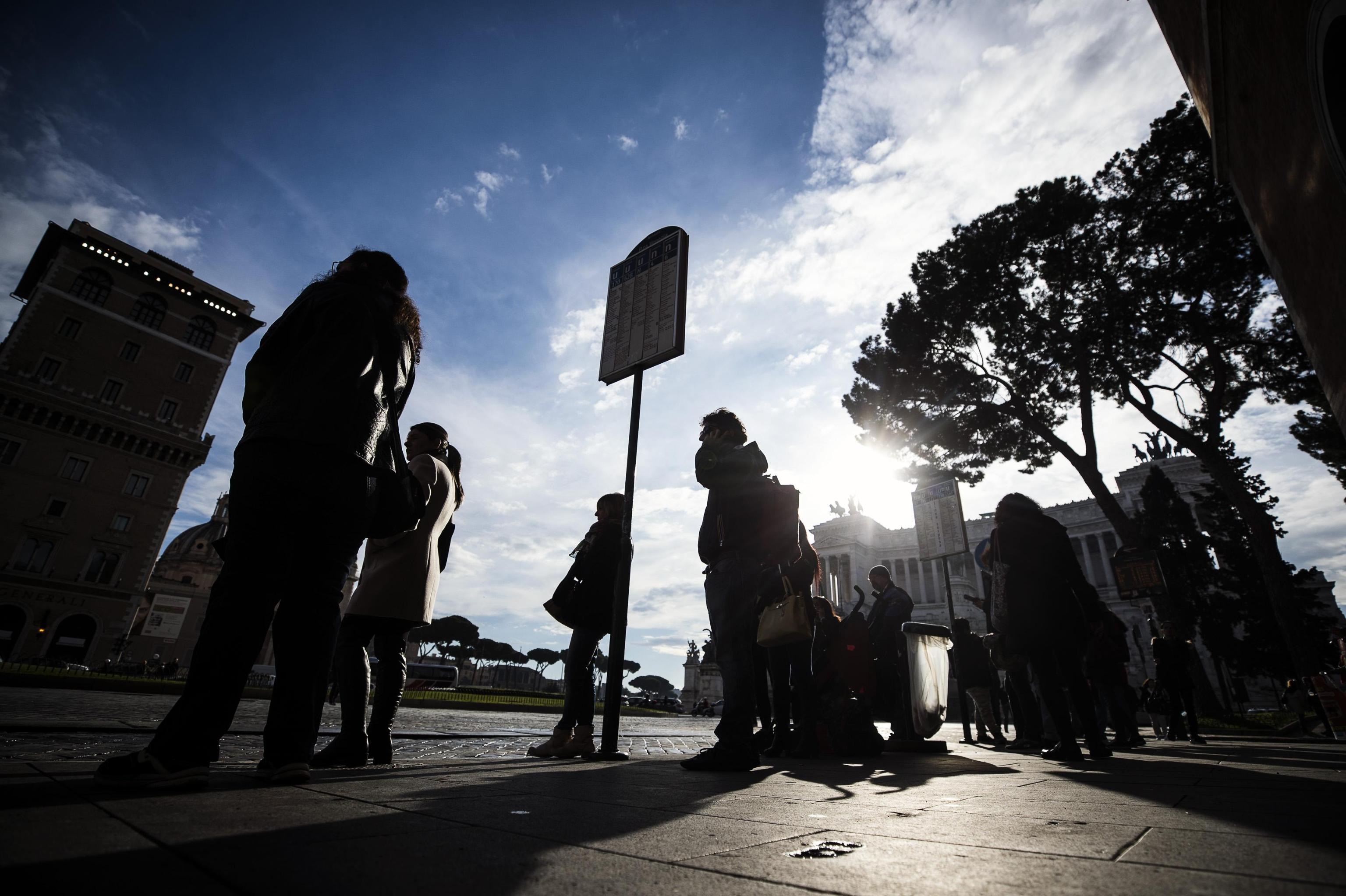 Alcune persone aspettano l'autobus alla fermata di Piazza Venezia a Roma