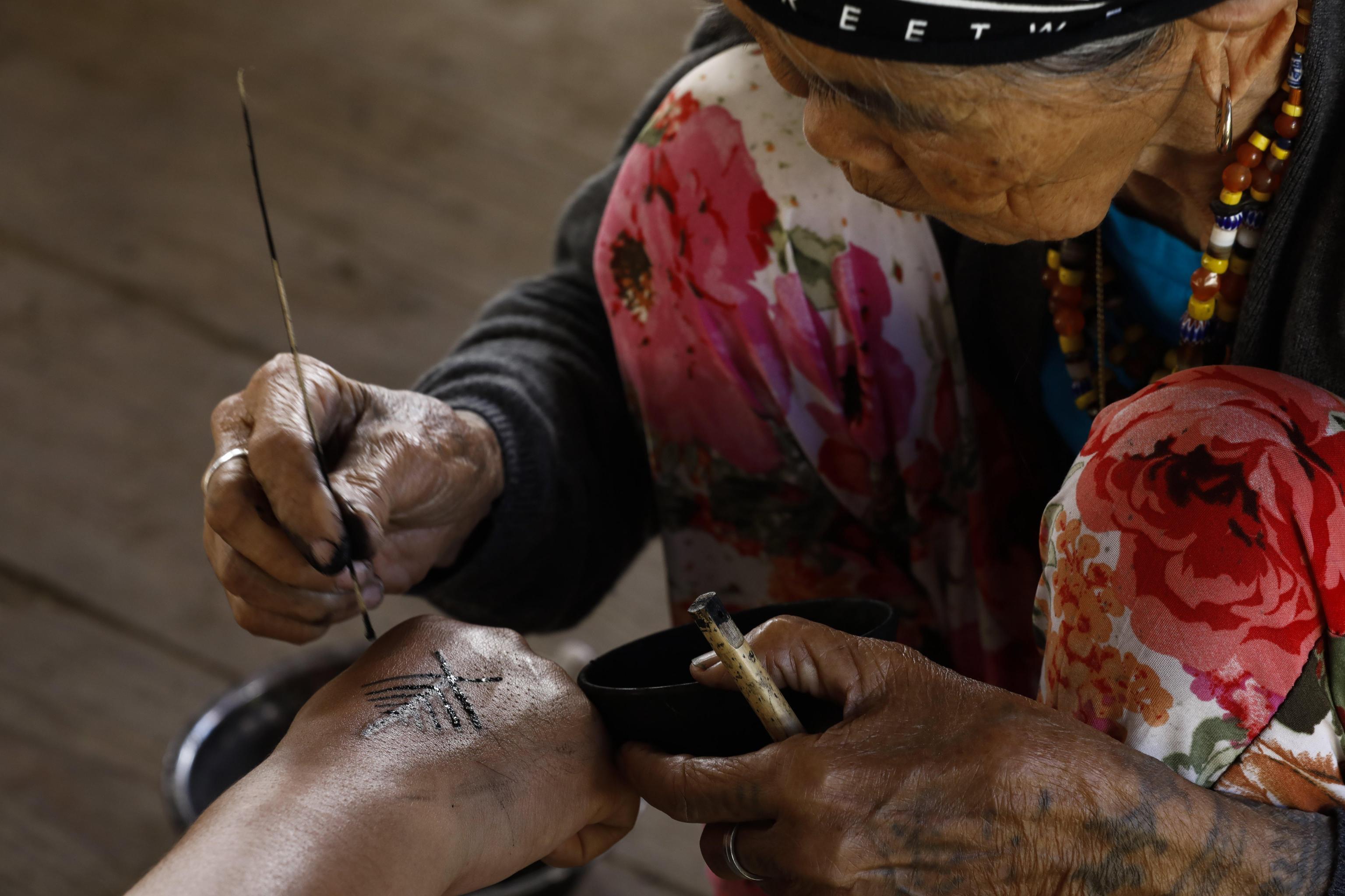Whang-od all’opera mentre con un pennellino traccia la linea del tatuaggio