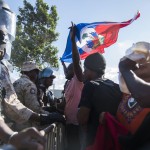 Un manifestante solleva la bandiera di Haiti di fronte ai soldati