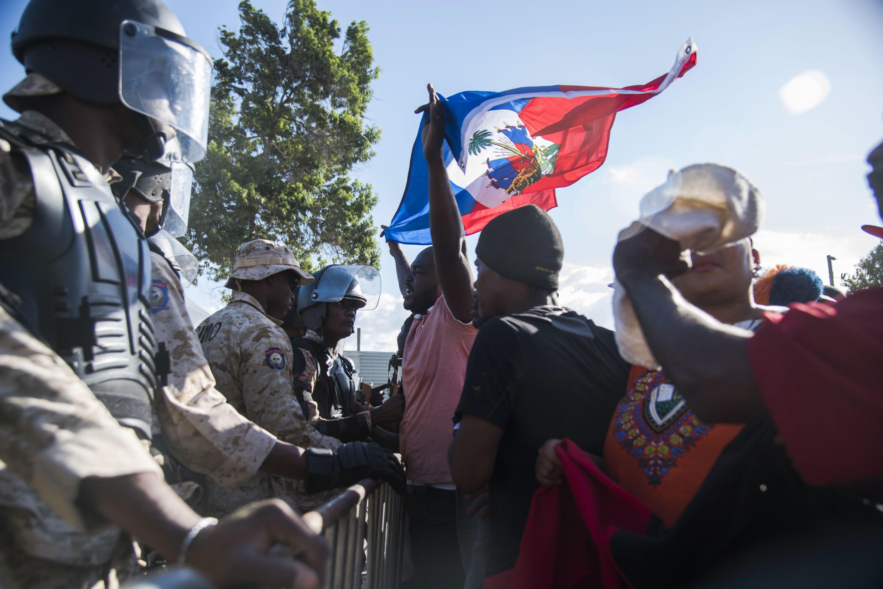 Un manifestante solleva la bandiera di Haiti di fronte ai soldati