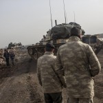 Due soldati turchi osservano il passaggio di due bambini in attesa di cominciare l’offensiva via terra in Siria