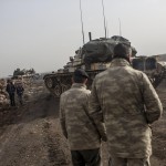 Due soldati turchi osservano il passaggio di due bambini in attesa di cominciare l’offensiva via terra in Siria