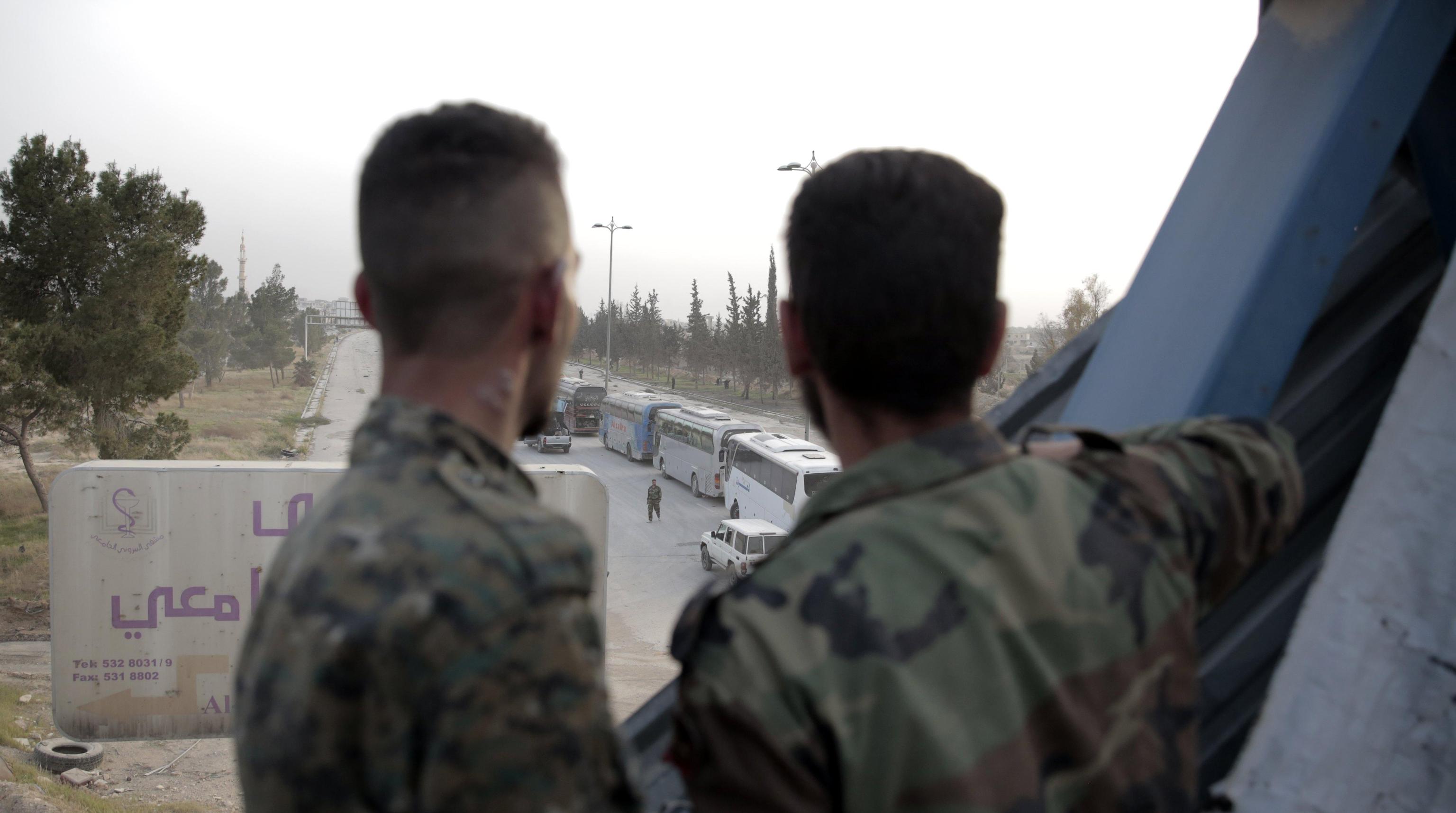 I soldati siriani guardano una linea di autobus noleggiati dal governo