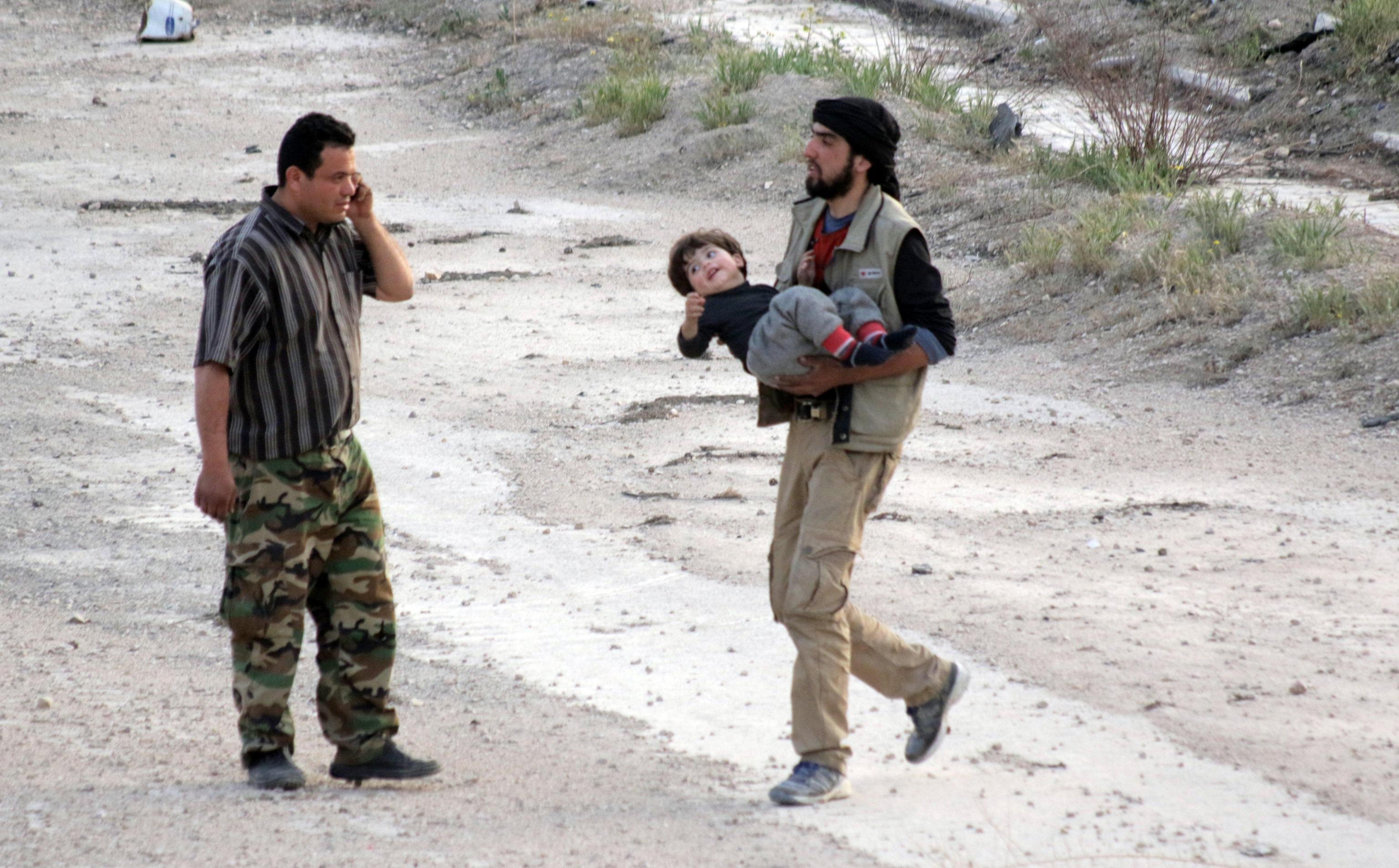 Un uomo della città di Harasta, detenuta dai ribelli, porta un bambino attraverso un corridoio sicuro