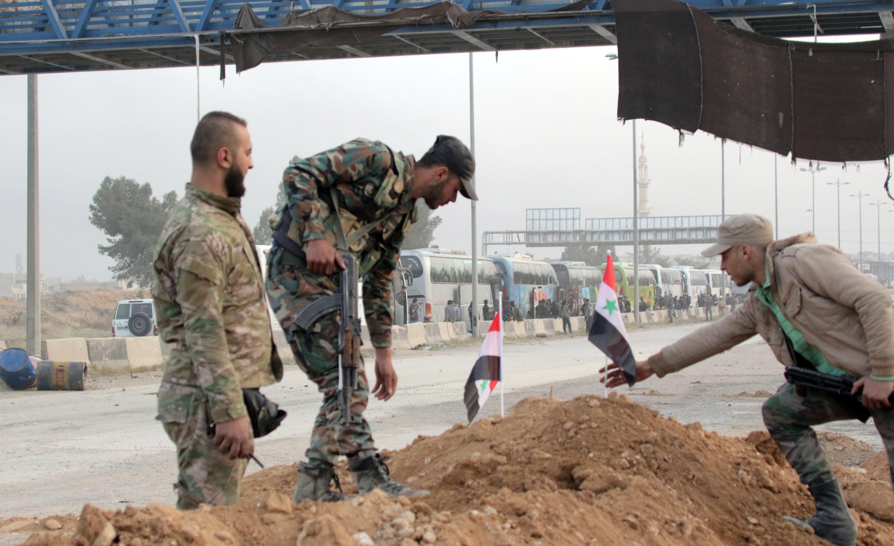 Soldati siriani posizionano piccole bandiere su un cumulo di terra, in attesa di partire