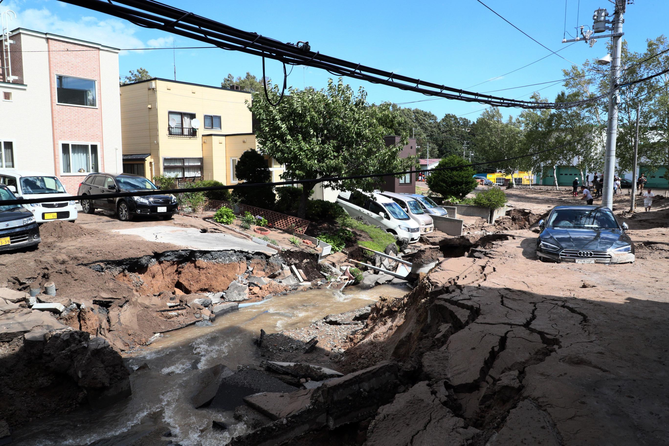 Macchine coperte dal fango in una strada distrutta dal terremoto