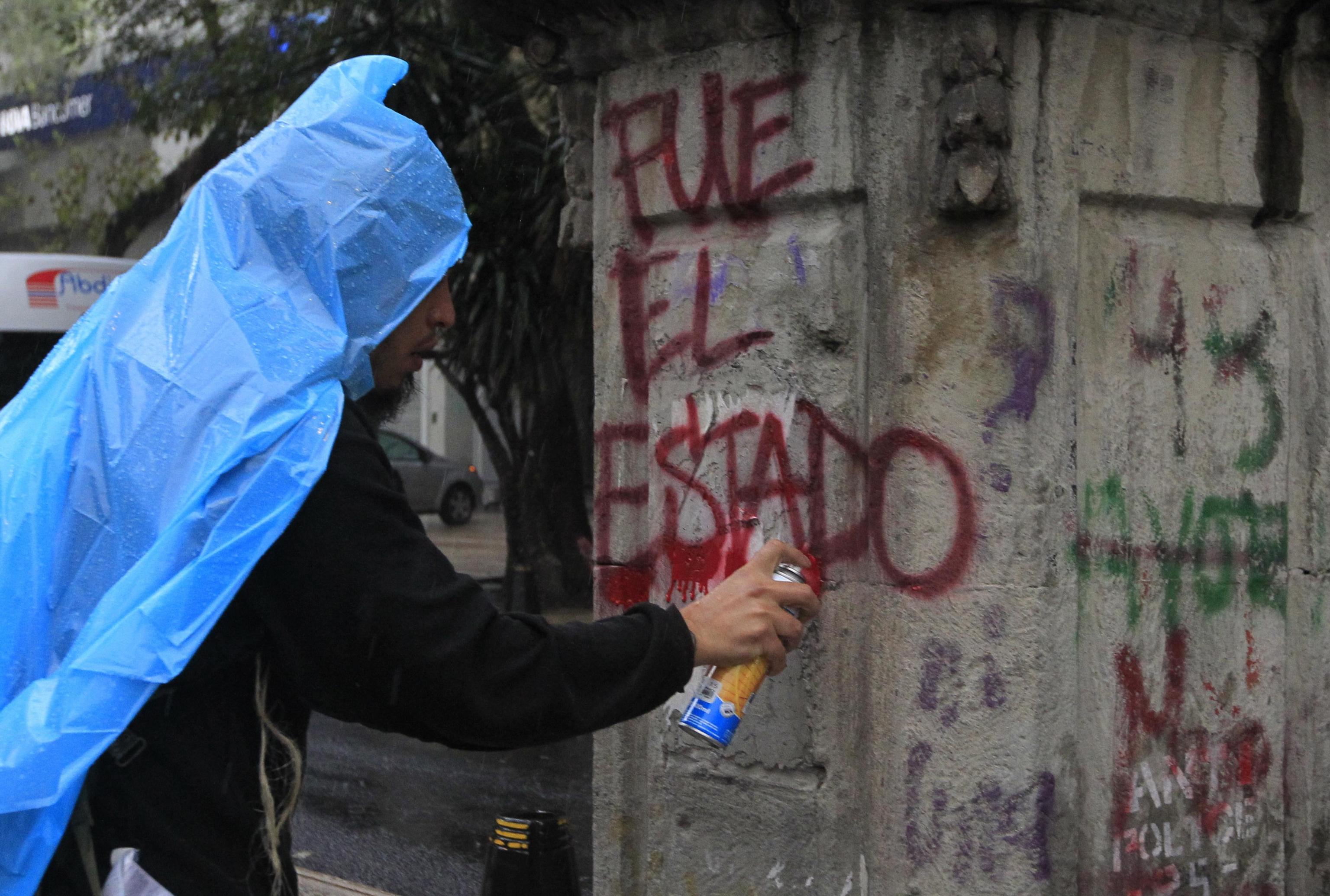 Un manifestante scrive su un muro "E' stato lo Stato", in relazione alla scomparsa degli studenti Un manifestante scrive su un muro "E' stato lo Stato", in relazione alla scomparsa degli studenti