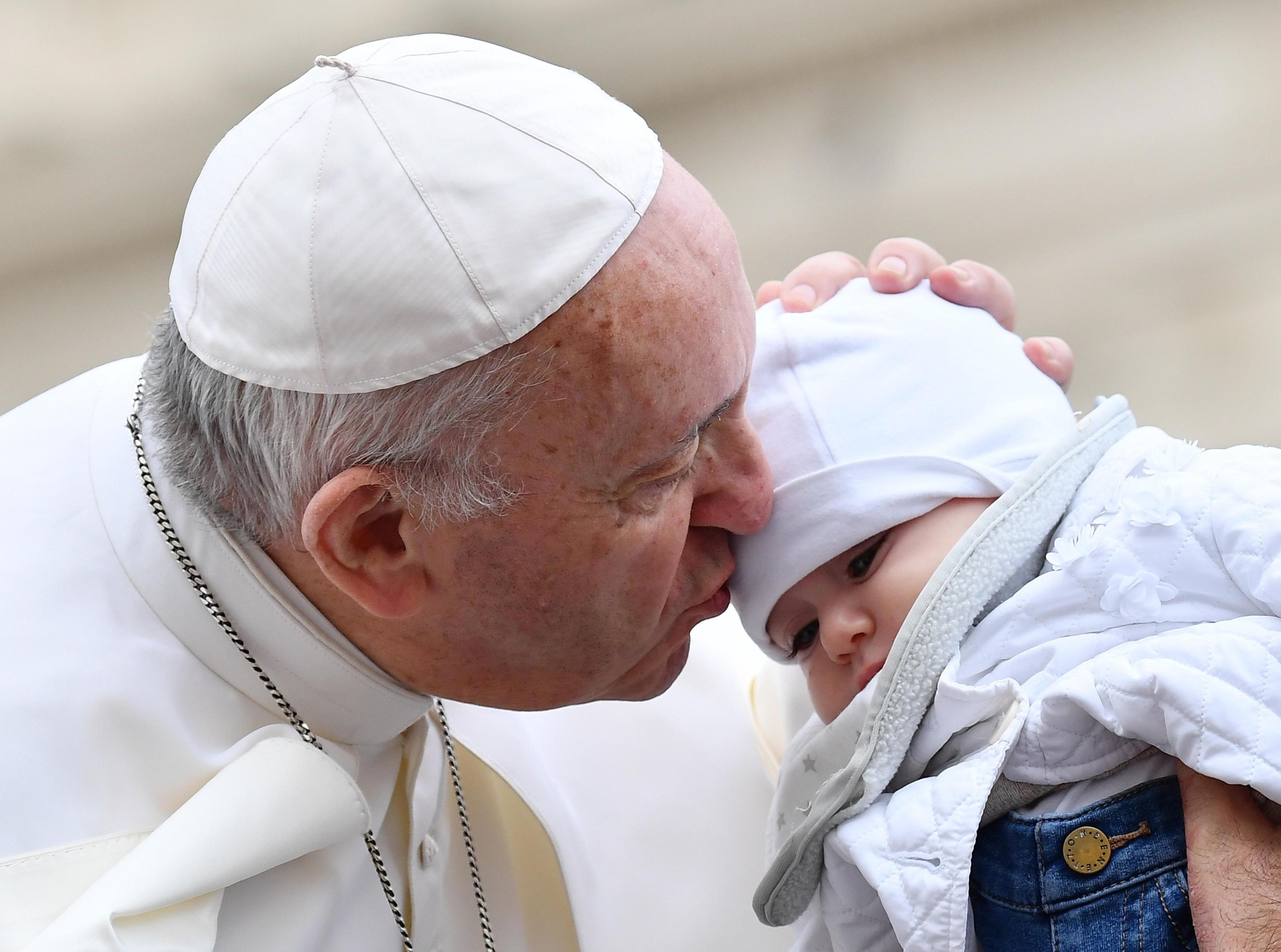 Papa Francesco bacia un bambino al suo arrivo a San Pietro durante il consueto giro in papamobile.