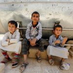 Bambini seduti accanto al serbatoio d'acqua contaminato.