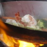 Gamberi e verdure cotti dalla chef in padella sua una stufa a carbone