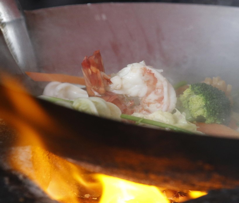 Gamberi e verdure cotti dalla chef in padella sua una stufa a carbone
