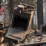 Una bandiera americana continua a sventolare sullo sfondo di un camper bruciato a Magalia (Contea di Butte, California)
