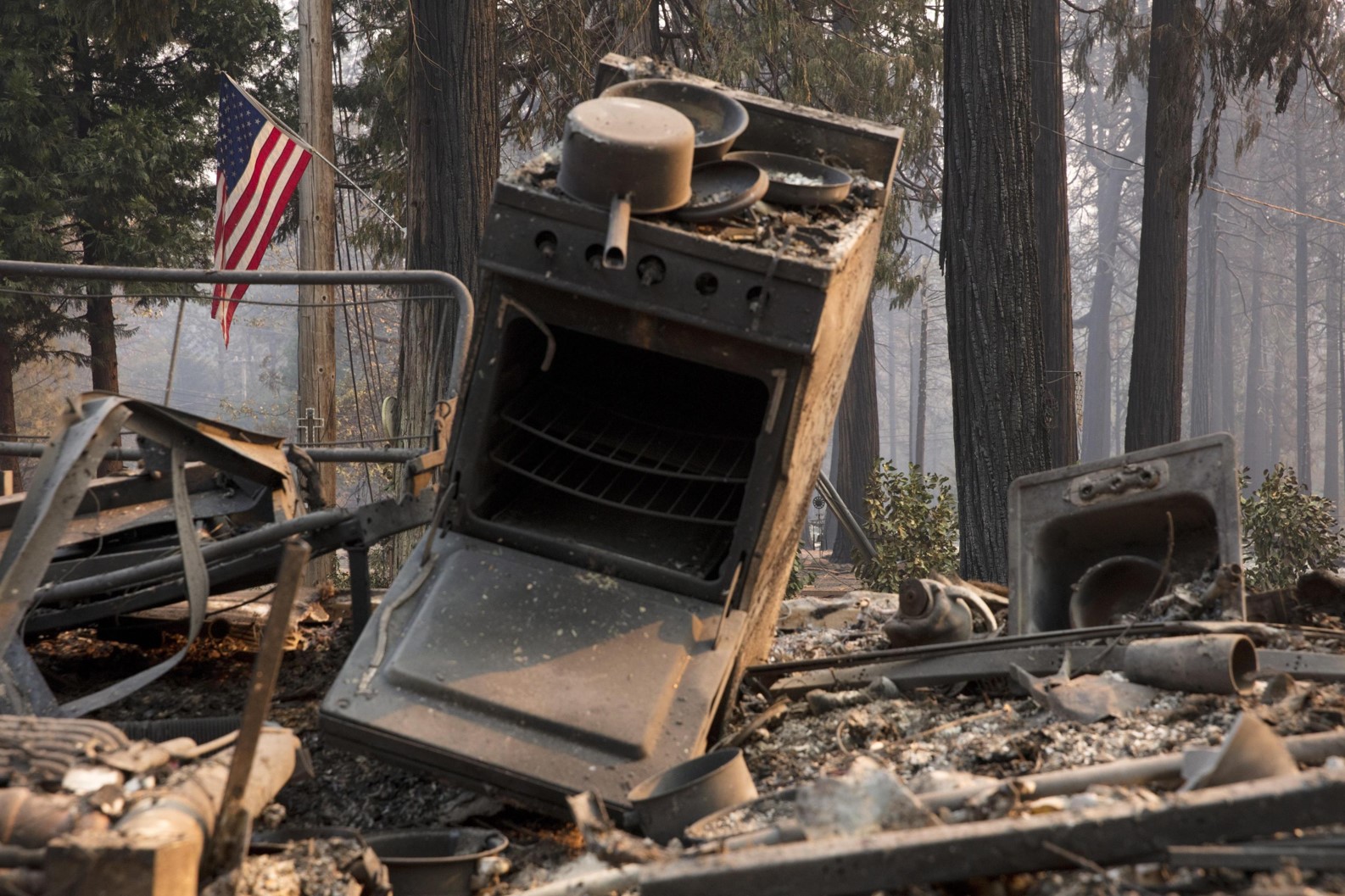 Una bandiera americana continua a sventolare sullo sfondo di un camper bruciato a Magalia (Contea di Butte, California)