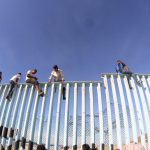 I migranti oltrepassano il recinto che divide i due Paesi