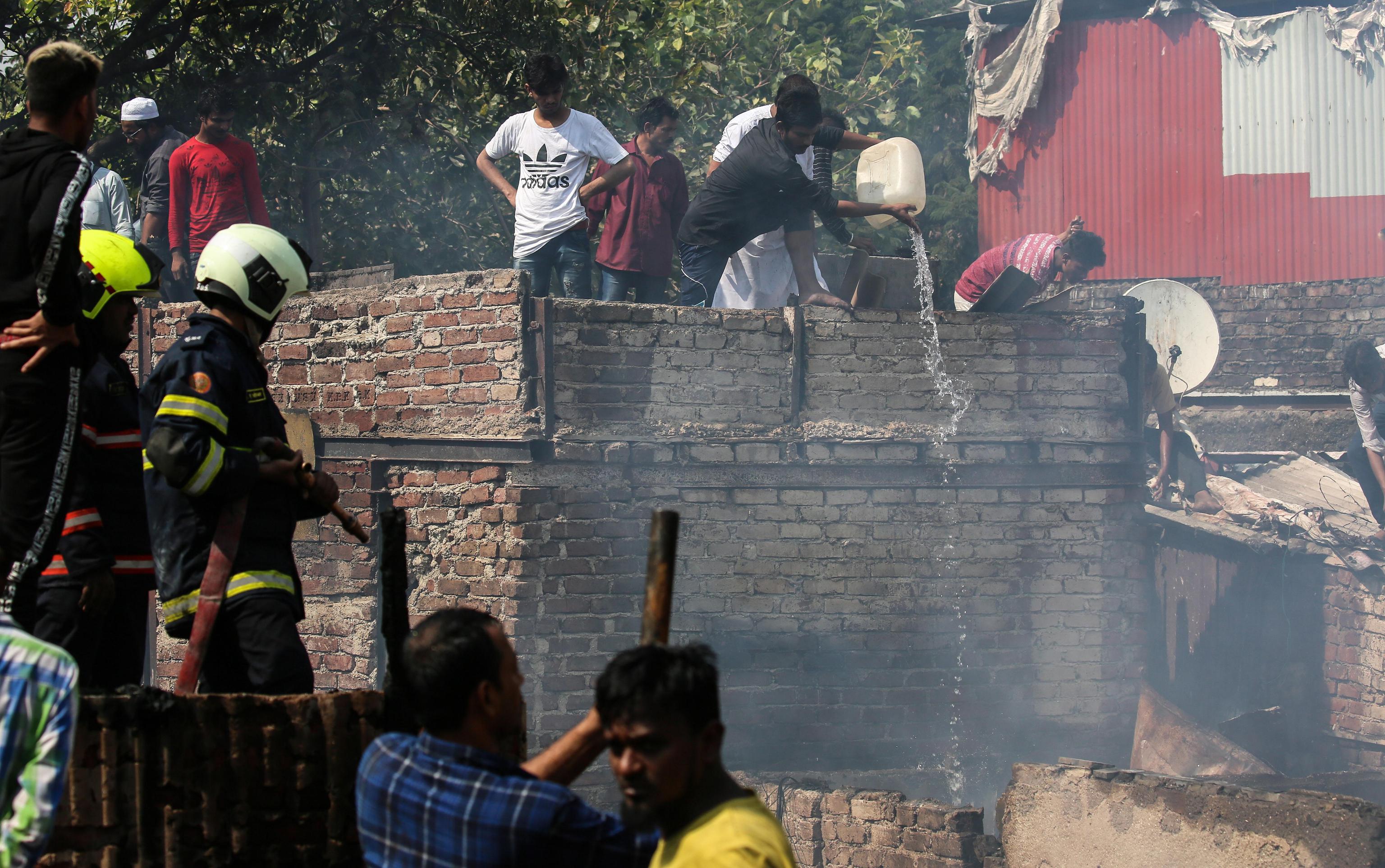 Gli abitanti delle capanne aiutano i vigili del fuoco locali a spegnere l'incendio che ha distrutto la baraccopoli