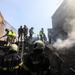 Gli abitanti delle capanne distrutte dall'incendio osservano i vigili del fuoco che continuano a lavorare
