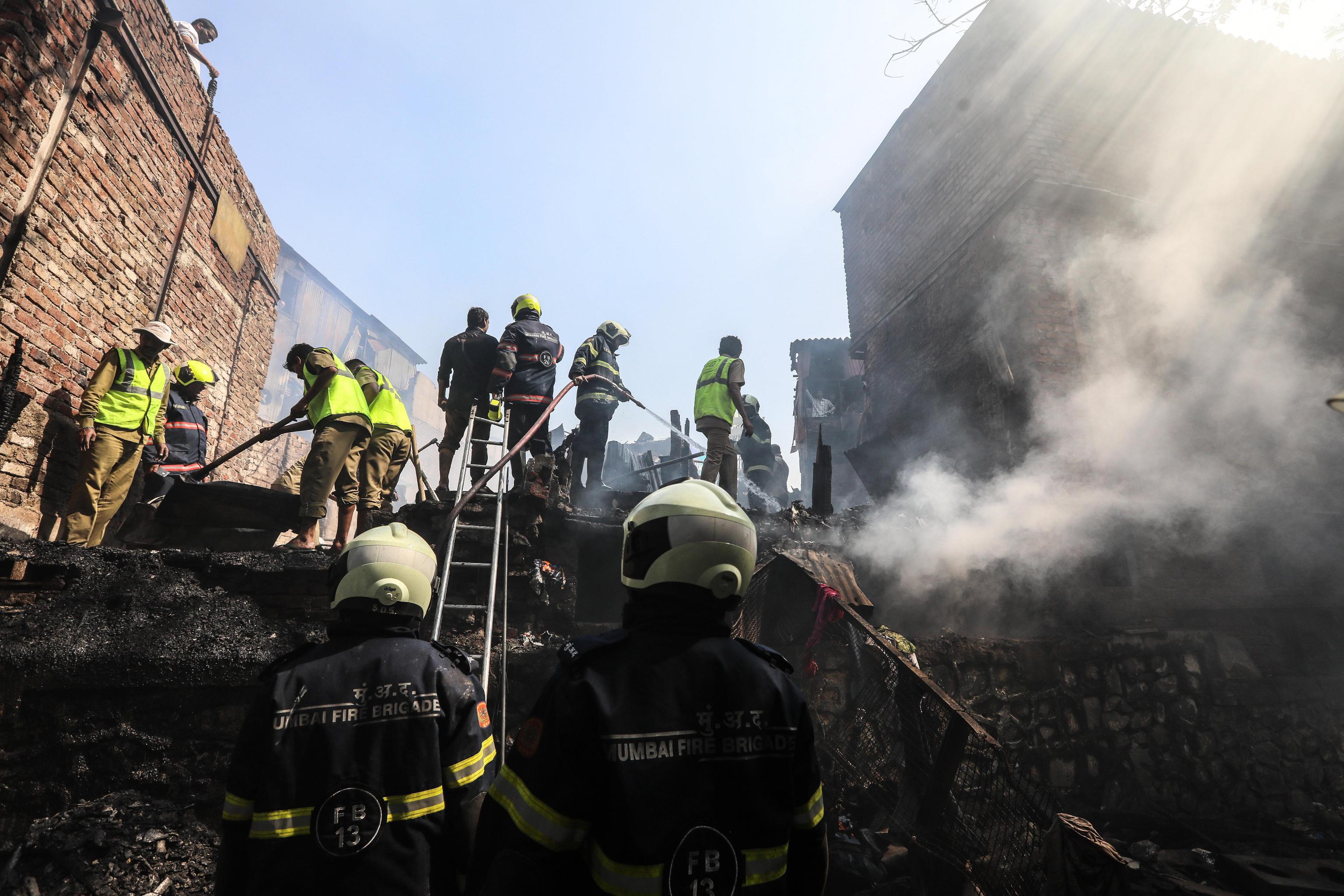 Gli abitanti delle capanne distrutte dall'incendio osservano i vigili del fuoco che continuano a lavorare