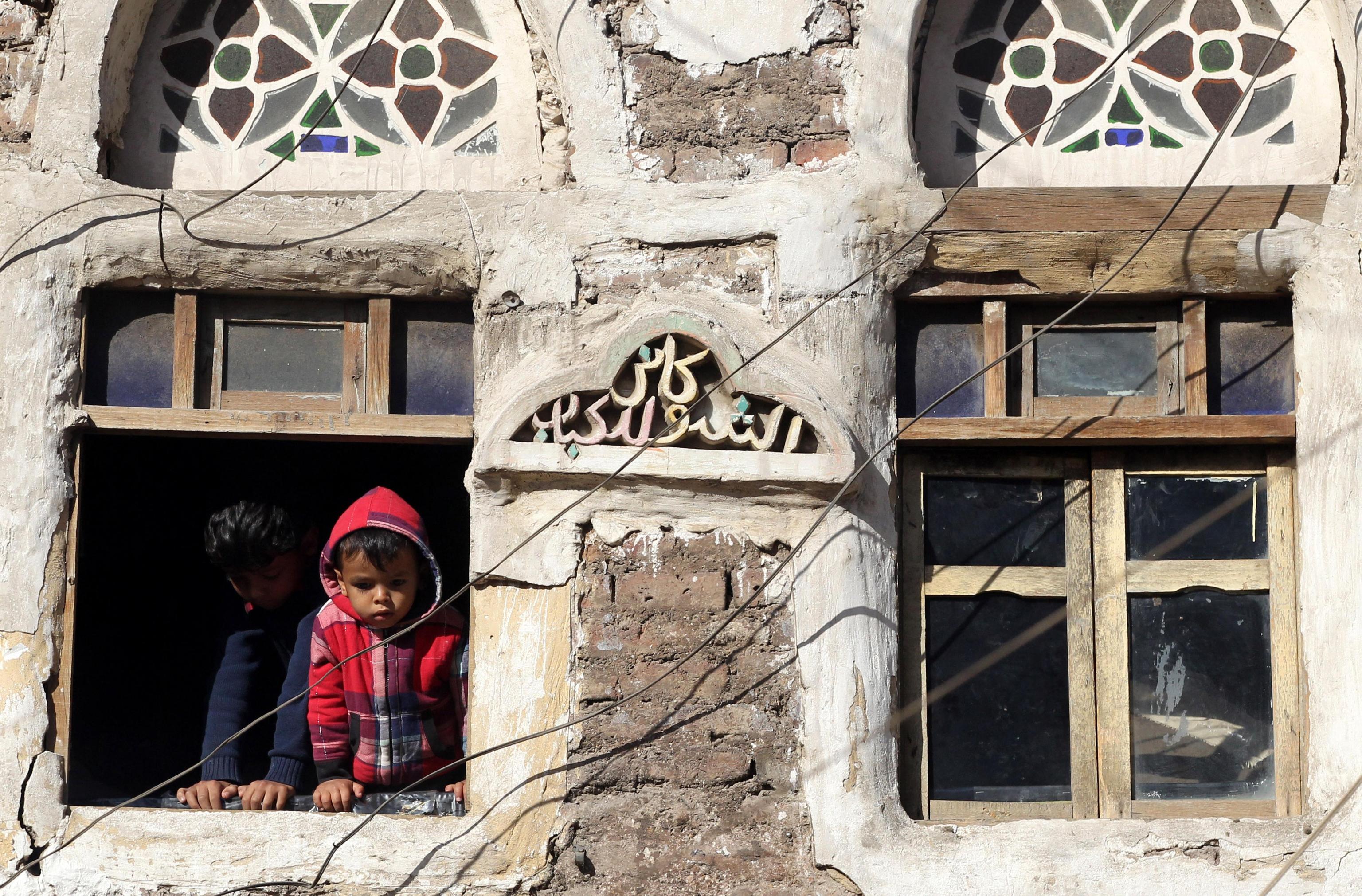 Due bambini sono affacciati ad una finestra, guardando la folla passare.