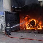 Un vigile del fuoco tenta di spegnere un veicolo dato in fiamme dai manifestanti