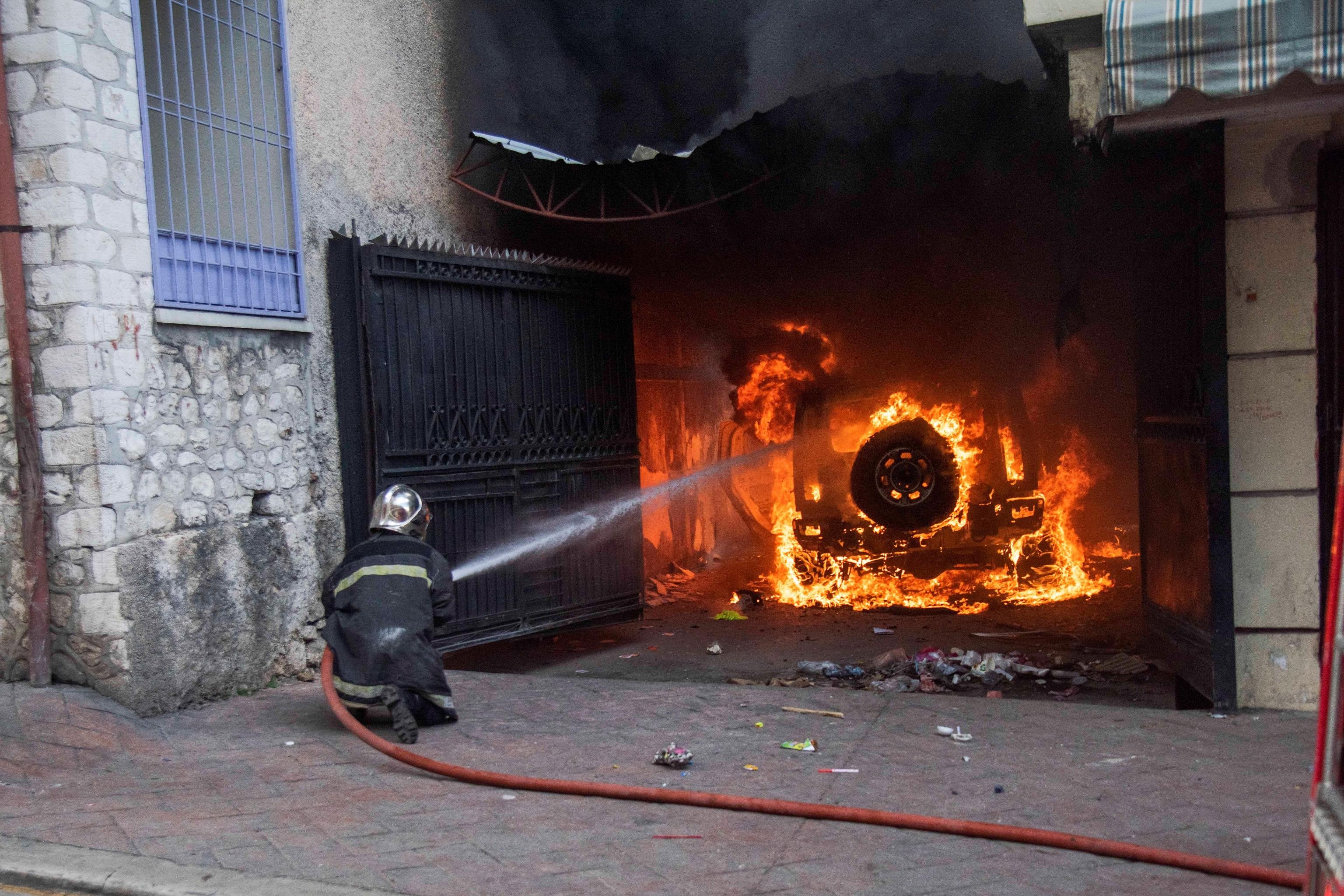 Un vigile del fuoco tenta di spegnere un veicolo dato in fiamme dai manifestanti