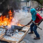 Un manifestante a volto coperto incendia pneumatici e insegne in protesta contro il presidente Moise