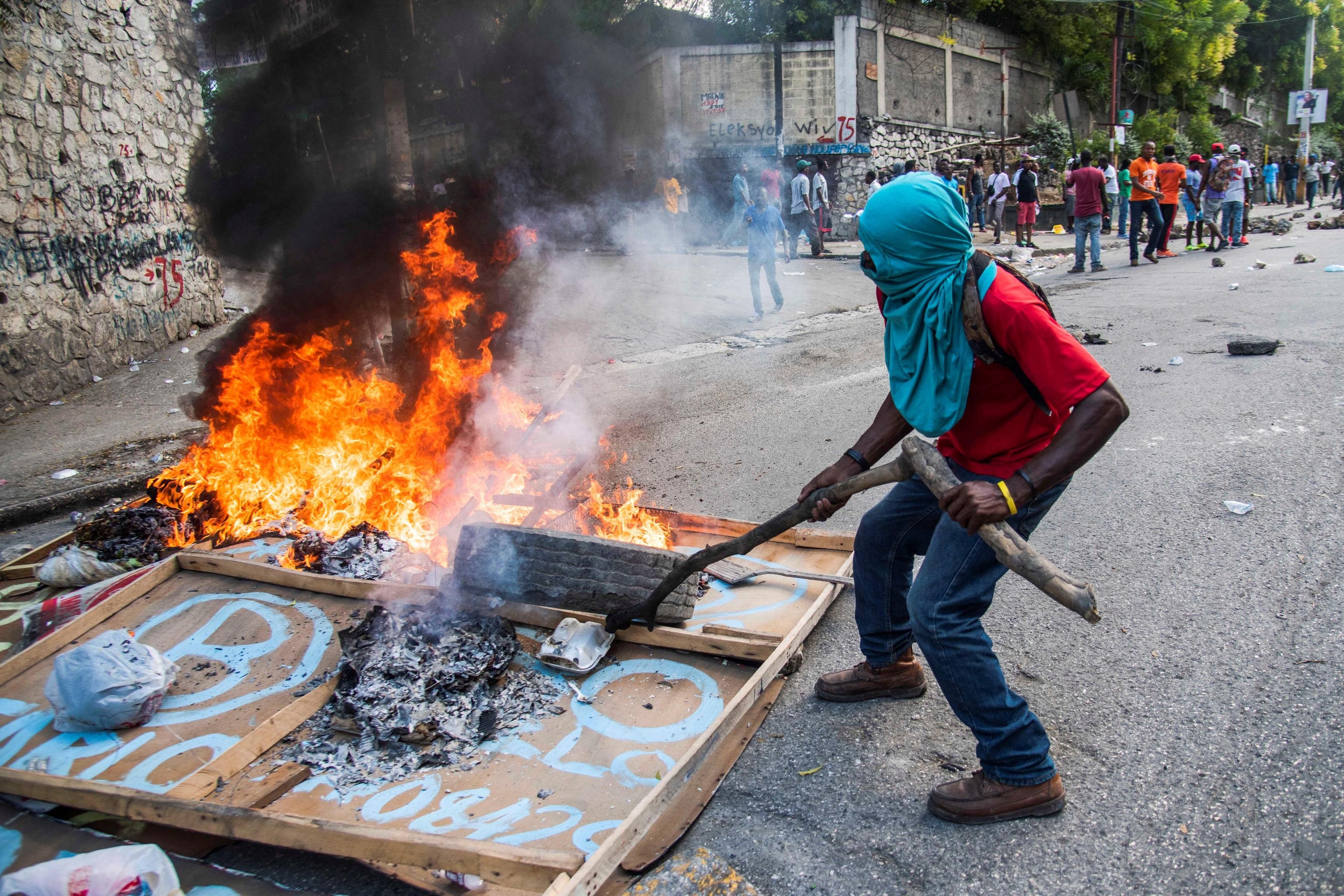 Un manifestante a volto coperto incendia pneumatici e insegne in protesta contro il presidente Moise