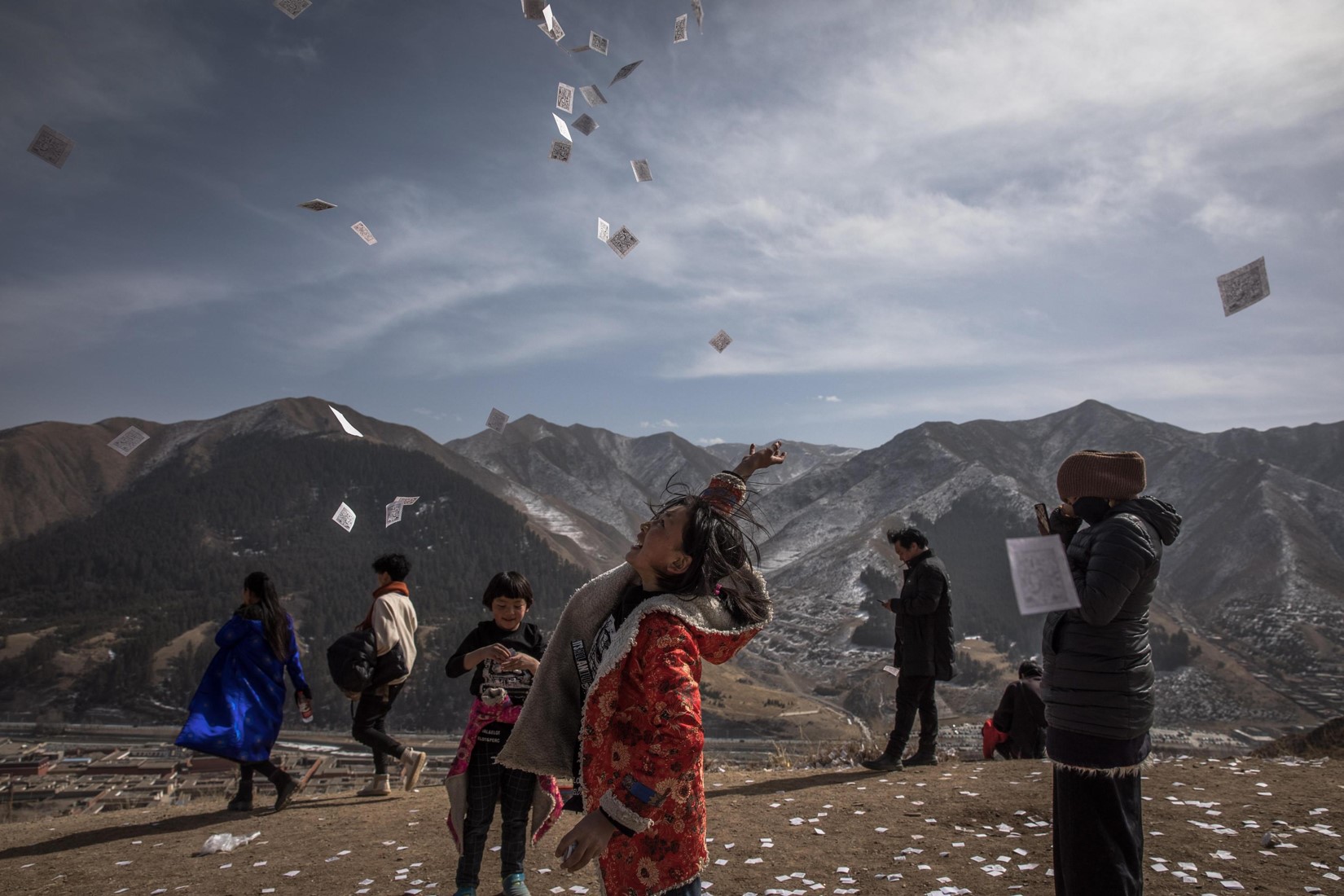 Una ragazza tibetana getta in aria un foglio con preghiere e speranze vicino al monastero di Labrang