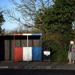 Una donna aspetta l'autobus ad una fermata dipinta con i colori degli unionisti vicino al confine Una donna aspetta l'autobus ad una fermata dipinta con i colori degli unionisti vicino al confine