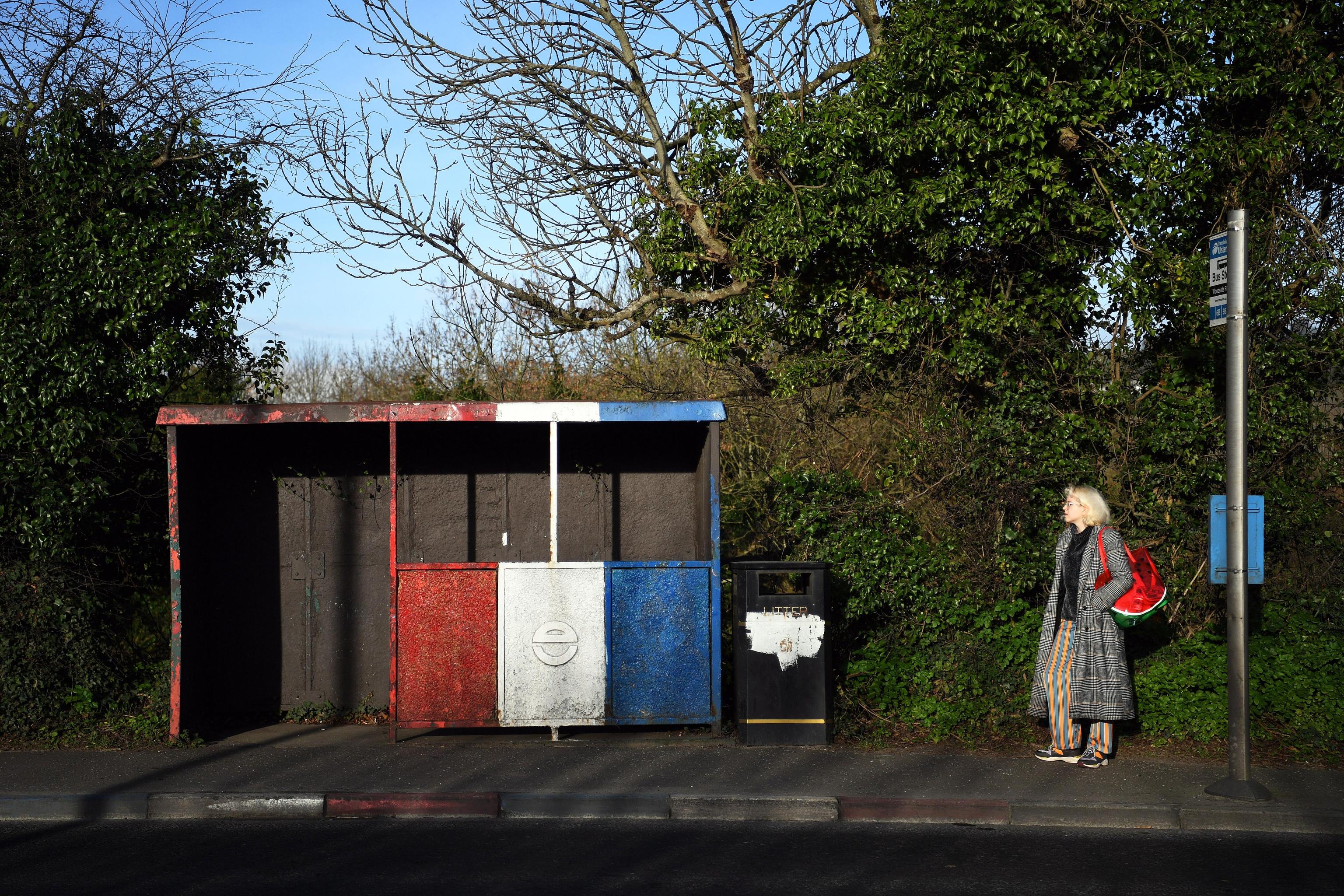 Una donna aspetta l'autobus ad una fermata dipinta con i colori degli unionisti vicino al confine
