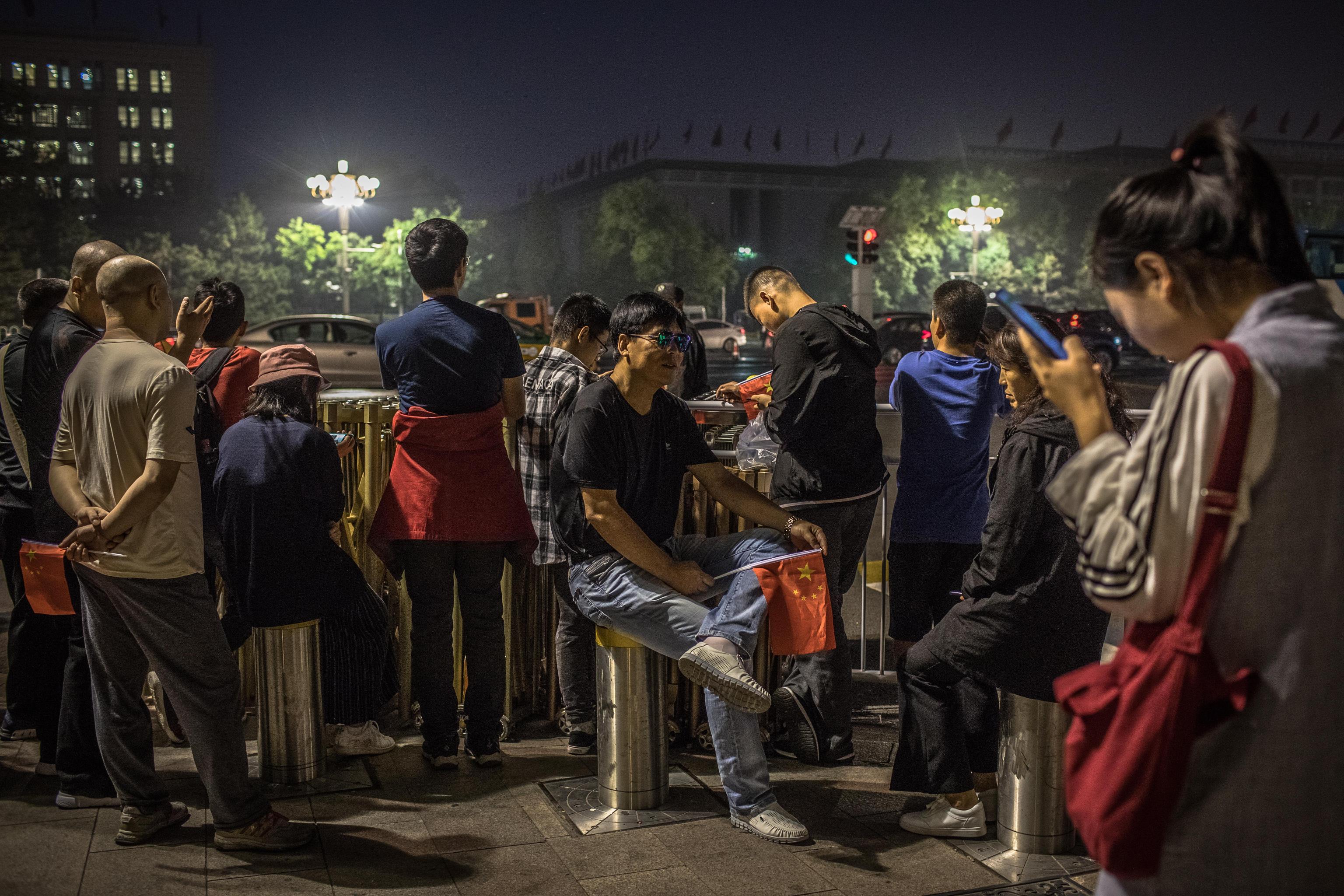 Alcuni cittadini cinesi attendono di assistere alla cerimonia di innalzamento della bandiera