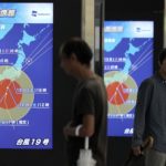 Passeggeri in attesa del treno sono davanti ad alcuni display che mostrano l'intensità del tifone