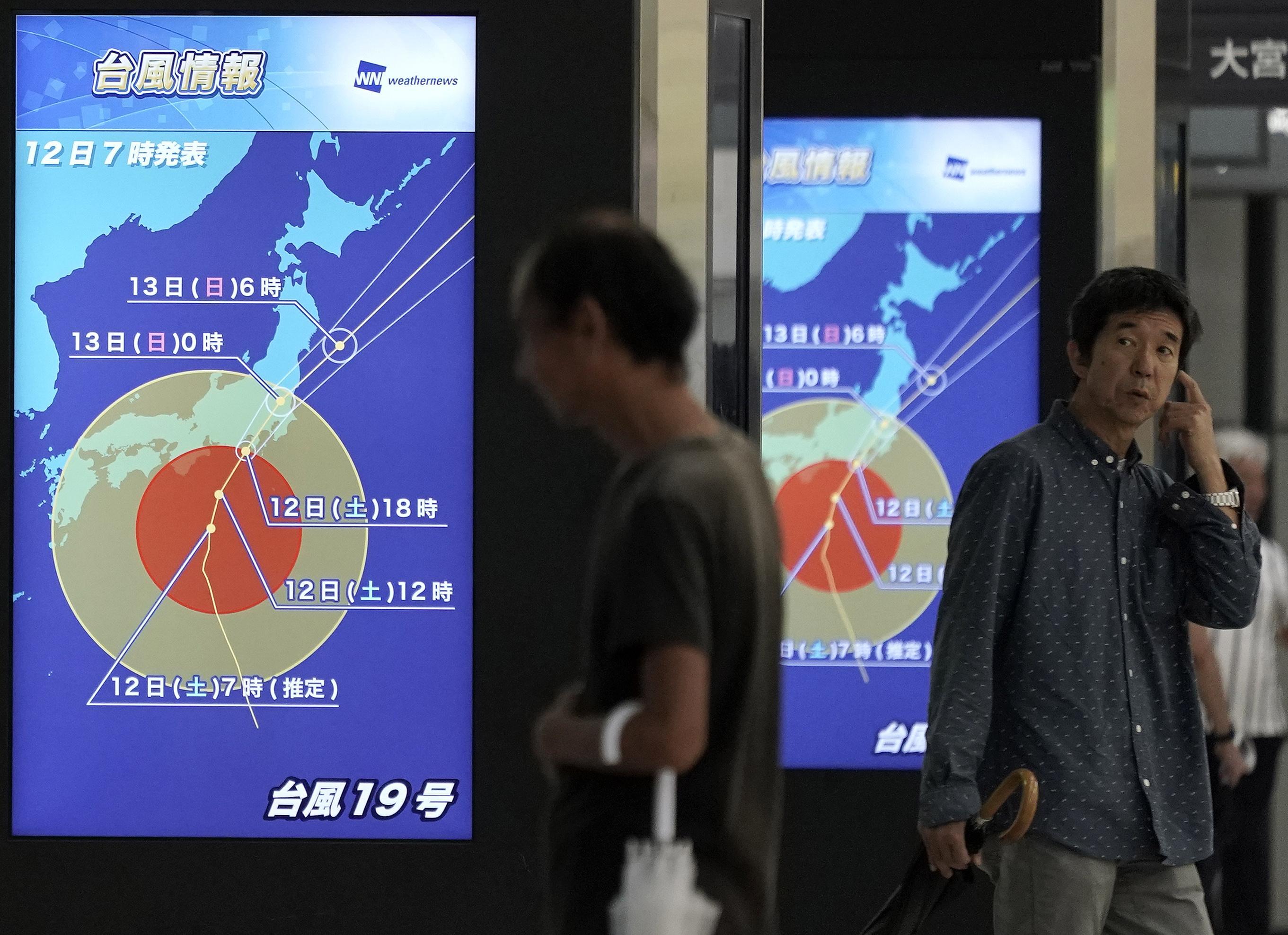 Passeggeri in attesa del treno sono davanti ad alcuni display che mostrano l'intensità del tifone