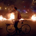 Un ciclista sperso fra le fiamme, guarda la devastazione delle proteste