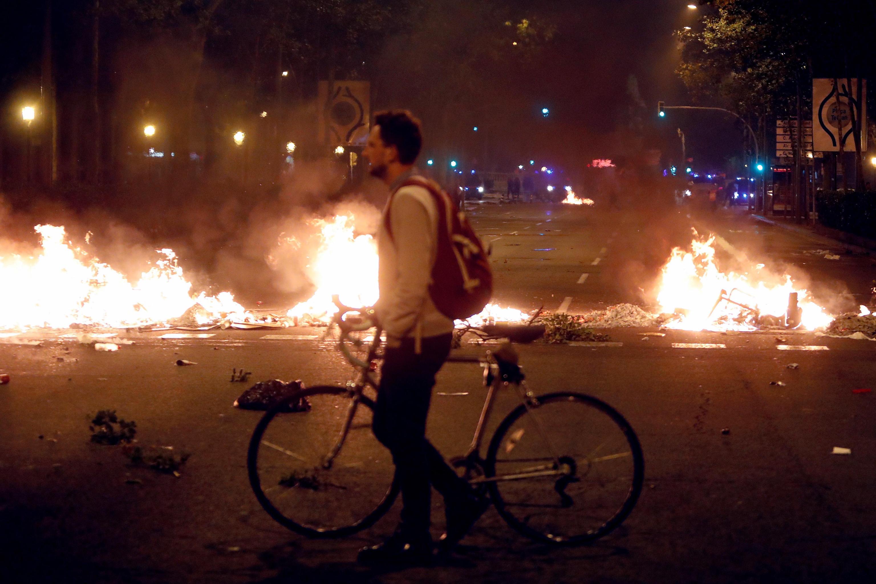 Un ciclista sperso fra le fiamme, guarda la devastazione delle proteste