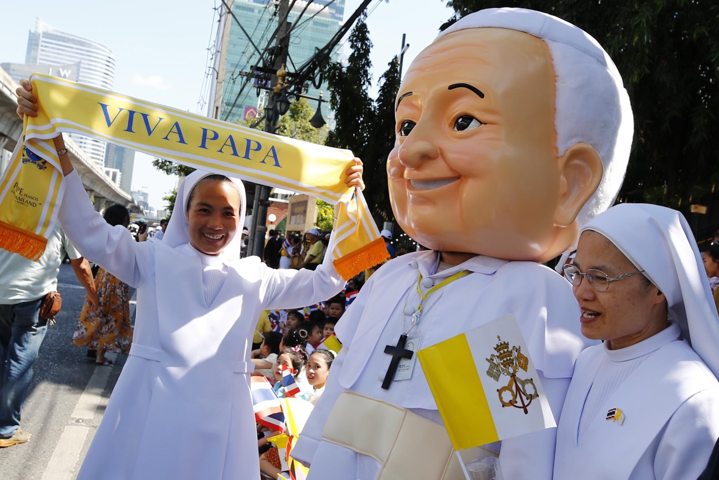 Un thailandese vestito con un costume di Papa Francesco sfila con delle suore con in mano una sciarpa che lo saluta