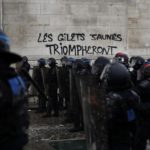 La polizia in marcia verso la manifestazione. Sullo sfondo la scritta:"I gilet gialli trionferanno" La polizia in marcia verso la manifestazione. Sullo sfondo la scritta:"I gilet gialli trionferanno"