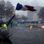 Un manifestante sventola la bandiera francese, sullo sfondo la polizia schierata Un manifestante sventola la bandiera francese, sullo sfondo la polizia schierata