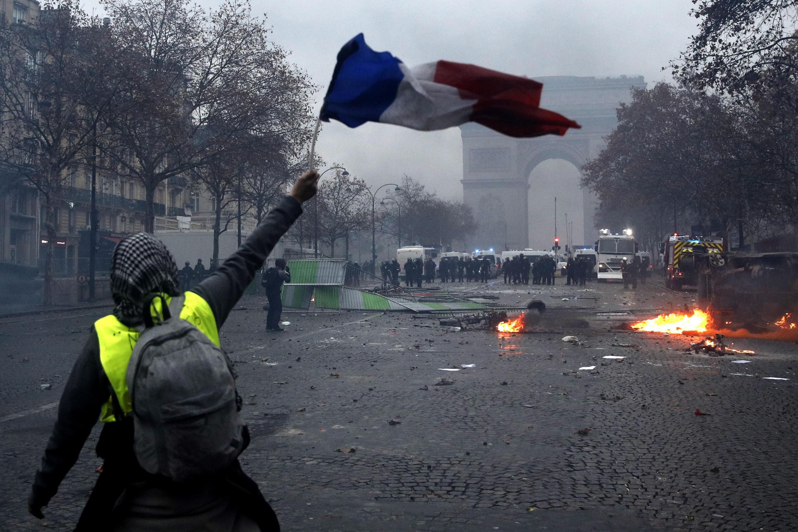 Un manifestante sventola la bandiera francese, sullo sfondo la polizia schierata Un manifestante sventola la bandiera francese, sullo sfondo la polizia schierata