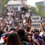 Un manifestante alza al cielo un cartello che chiede subito una nuova costituzione