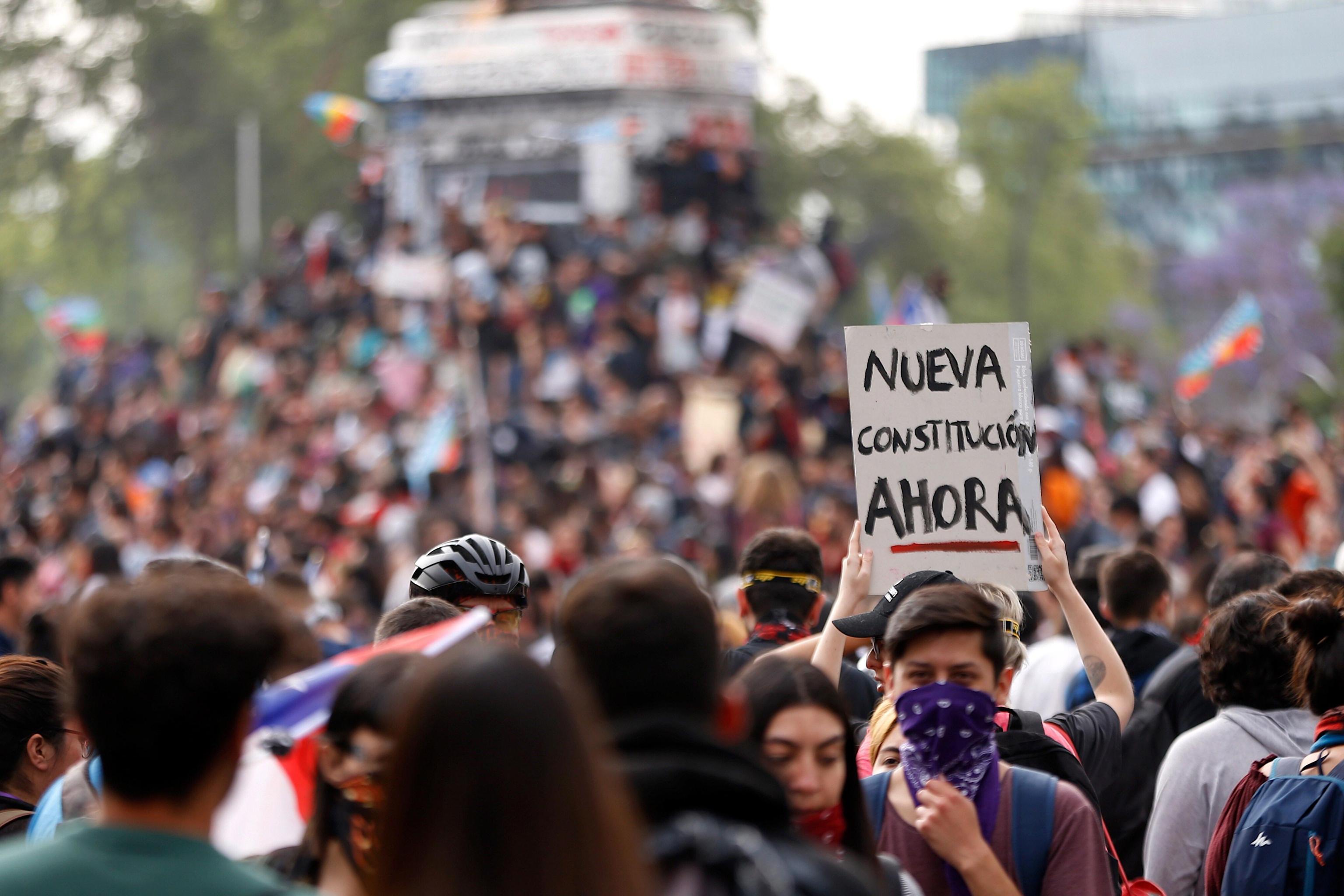 Un manifestante alza al cielo un cartello che chiede subito una nuova costituzione