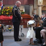 Il commissario dei vigili del fuoco guarda la figlia di un volontario mentre indossa l'elmetto del padre al suo funerale