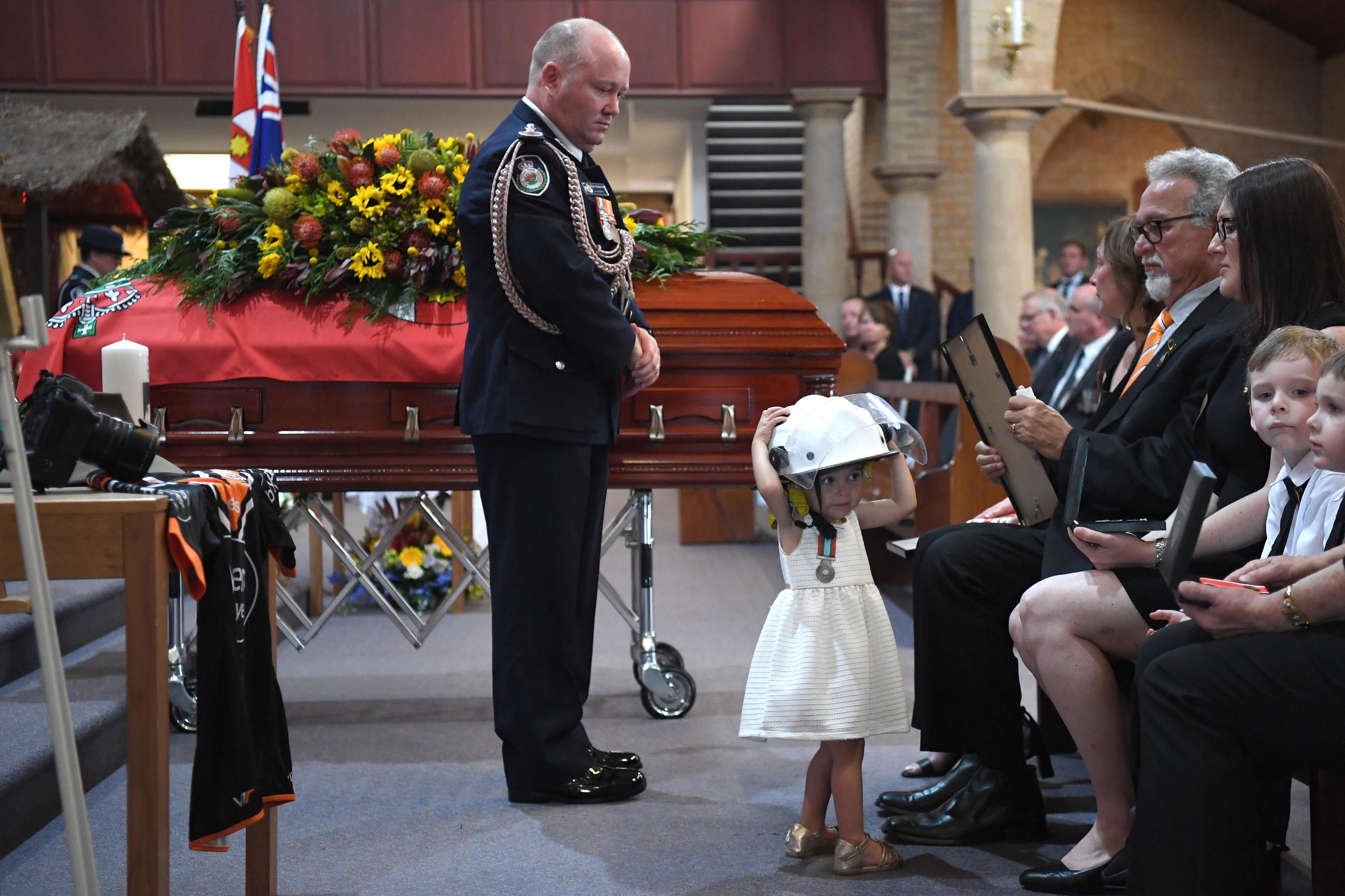 Il commissario dei vigili del fuoco guarda la figlia di un volontario mentre indossa l'elmetto del padre al suo funerale