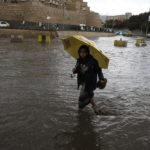 Un ragazzo yemenita con un ombrello guada attraverso una strada allagata nel vecchio quartiere della capitale yemenita