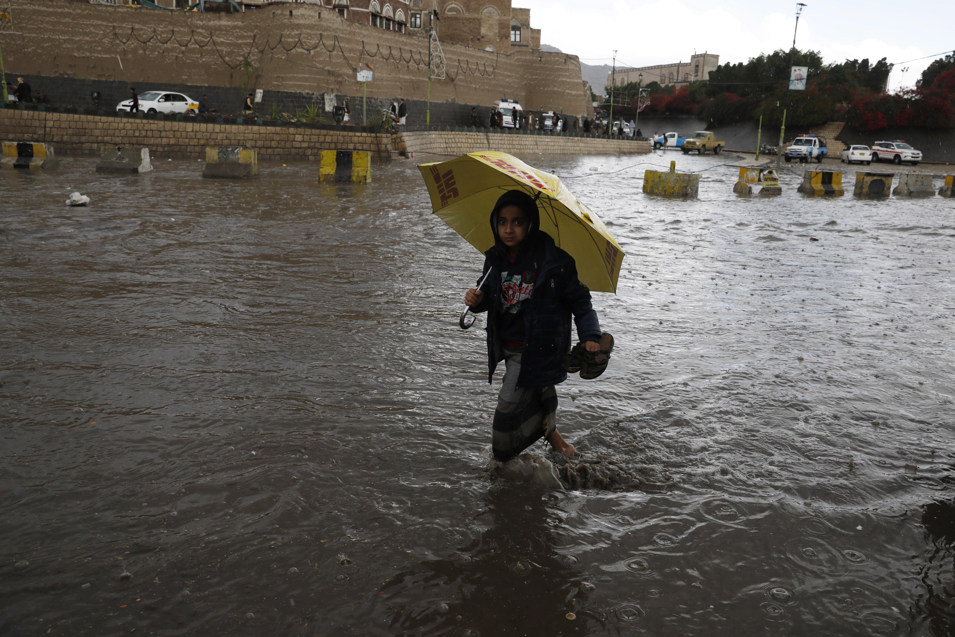 Un ragazzo yemenita con un ombrello guada attraverso una strada allagata nel vecchio quartiere della capitale yemenita