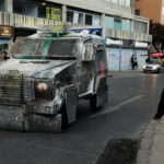 Un giocoliere da strada finge di sparare al blindato dei militari con una clava Un giocoliere da strada finge di sparare al blindato dei militari con una clava