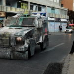 Un giocoliere da strada finge di sparare al blindato dei militari con una clava