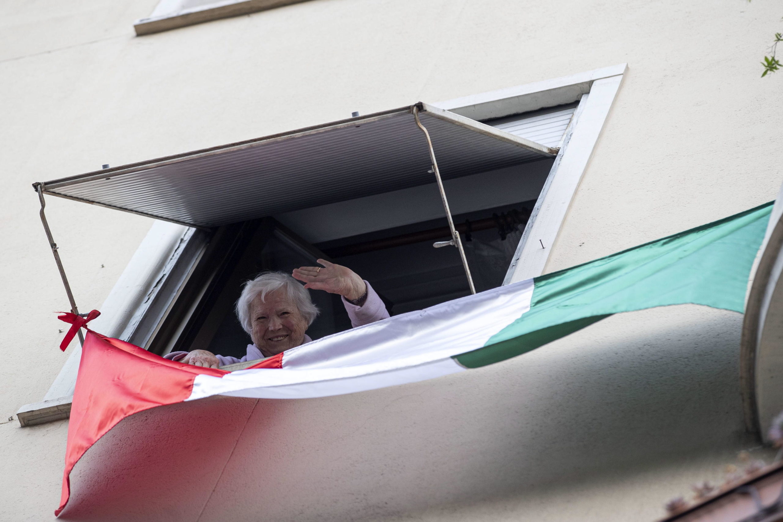 Una donna affacciata alla finestra a Roma saluta i giornalisti